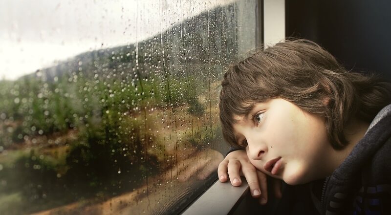 A sad kid looking out of a window tracked with rain. Because his video marketing isn't going well.